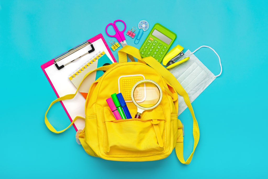 Back to school, education concept Yellow backpack with school supplies, protective medical mask, calculator, scissors isolated on blue background. Top view Copy space Flat lay.
