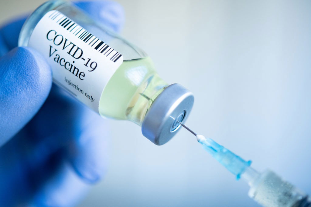 Preparing injection with covid-19 vaccine Doctor drawing up Covid-19 vaccine from glass phial bottle and filling syringe injection for vaccination. Close up of hand wearing protective disposable gloves in lab and holding a bottle of vaccination drugs. Hand with blue surgical gloves taking sars-coV-2 vaccine dose from vial with syringe: prevention and immunization concept.