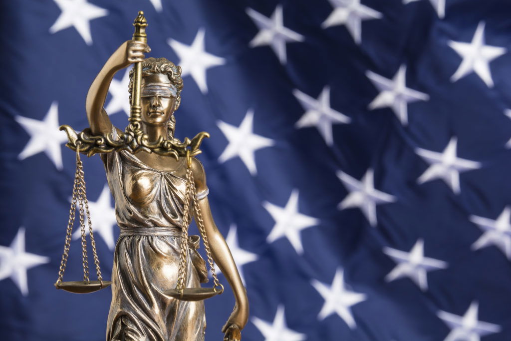 The statue of justice Themis or Justitia, the blindfolded goddess of justice against a flag of the United States of America, as a legal concept