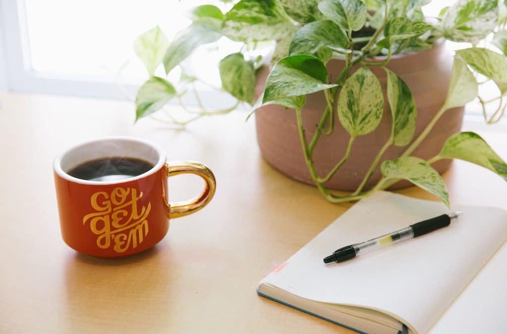 5 tips to improve your newsletter. Picture of plant, coffee, notebook and pen.