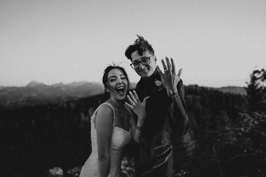 A couple shows off their wedding rings with joy on their faces. 