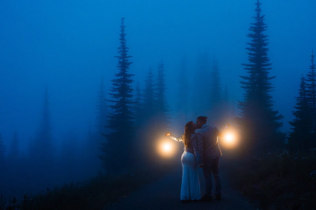 A couple kisses on a foggy day in the mountains holding lanterns