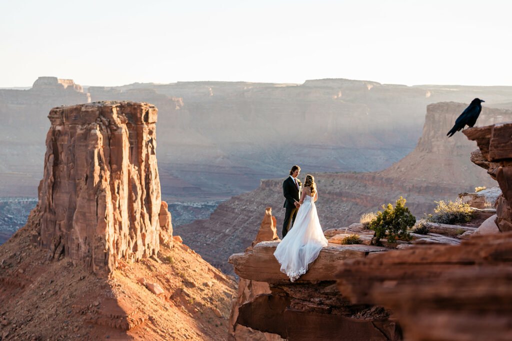 A couple stands at a beautiful vista in the desert at sunset.